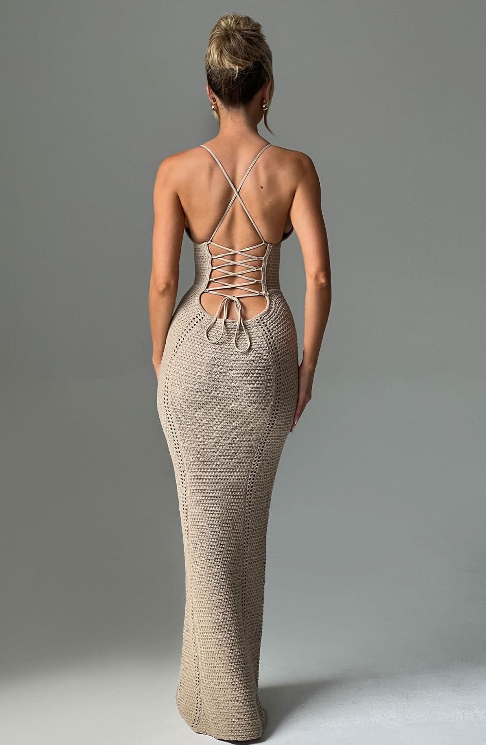 Back view of a woman in a beige crochet maxi dress, showing the detailed lace-up back and form-fitting silhouette.