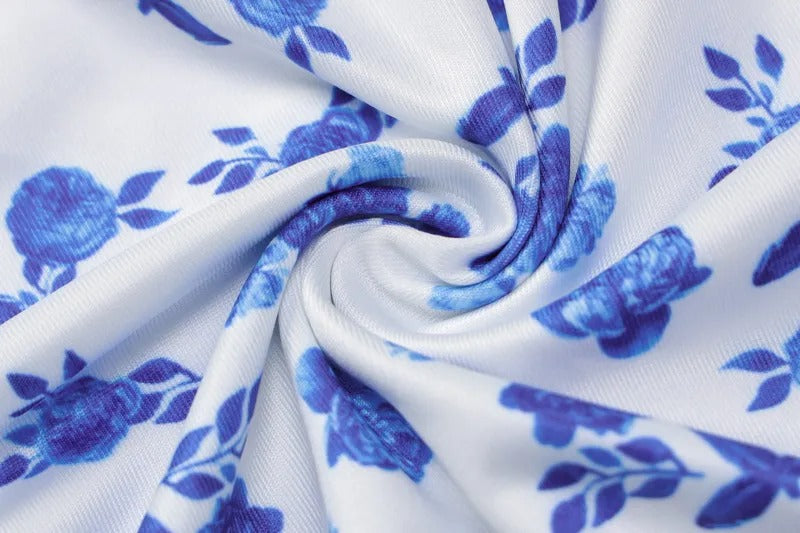 Close-up of the Brooke Floral Maxi Dress fabric, showing white material with vibrant blue floral and leaf patterns, detailed with soft folds.