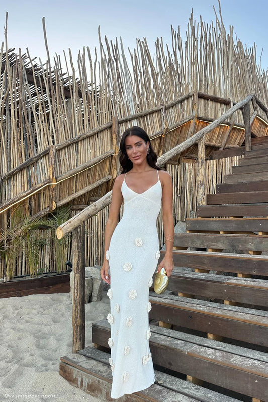 Chelsea Floral Maxi Dress in white, featuring delicate floral appliques and thin spaghetti straps, worn outdoors on wooden steps.