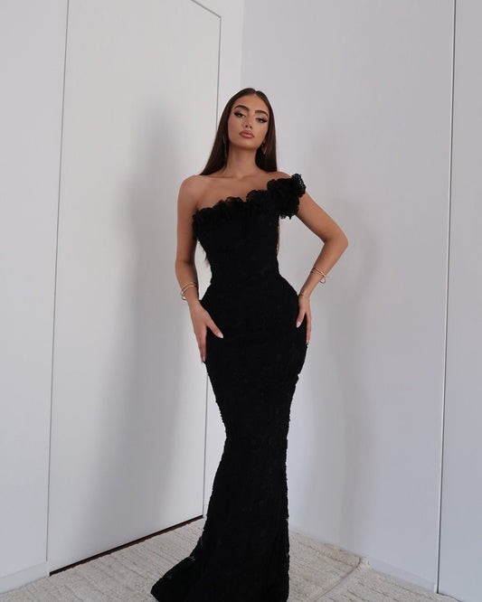 Full-length view of a woman wearing a black floral one-shoulder maxi dress for formal events.