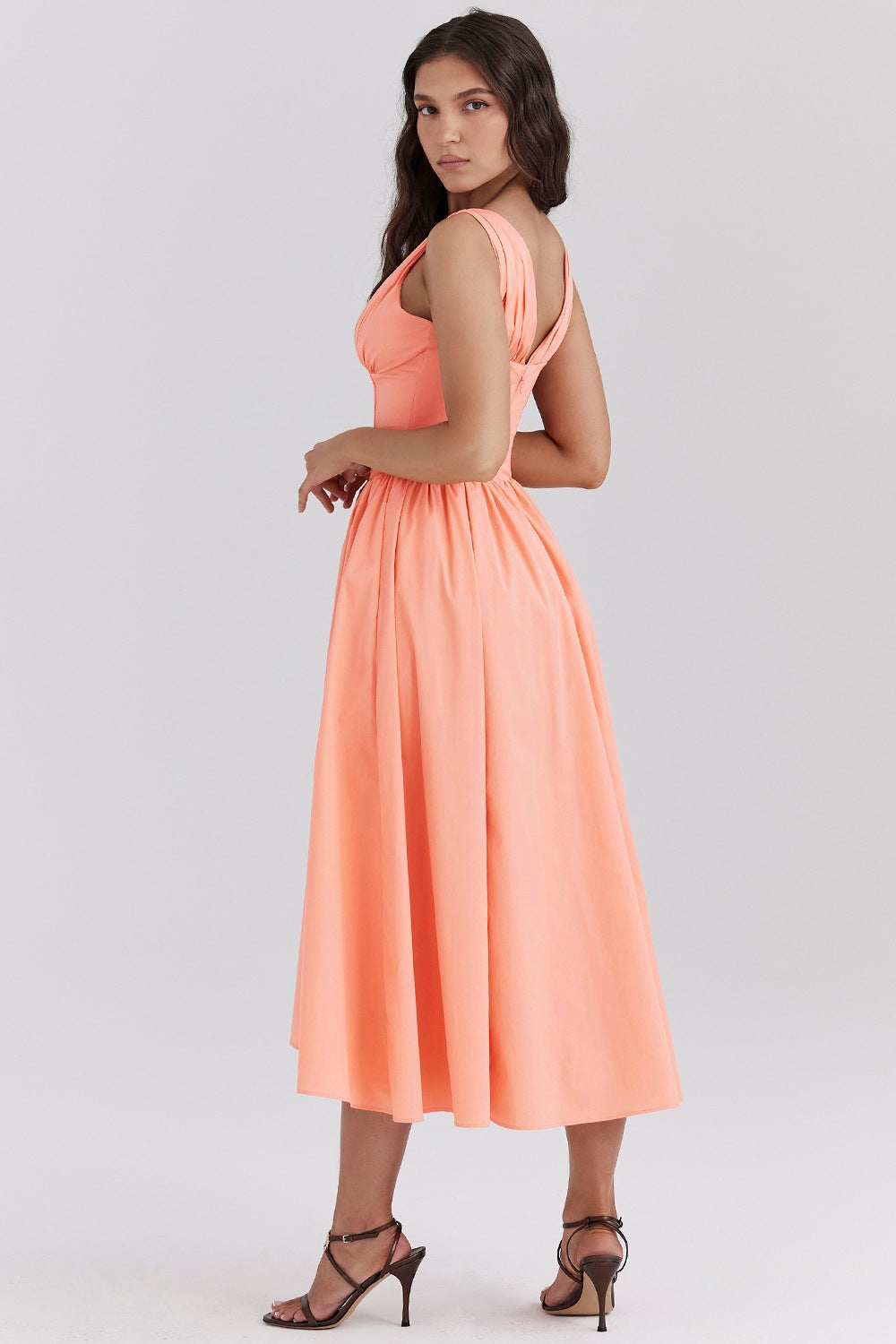 Peach midi dress with a fitted bodice and a full, pleated skirt, featuring wide shoulder straps and a v-neckline, worn with dark brown strappy heels.