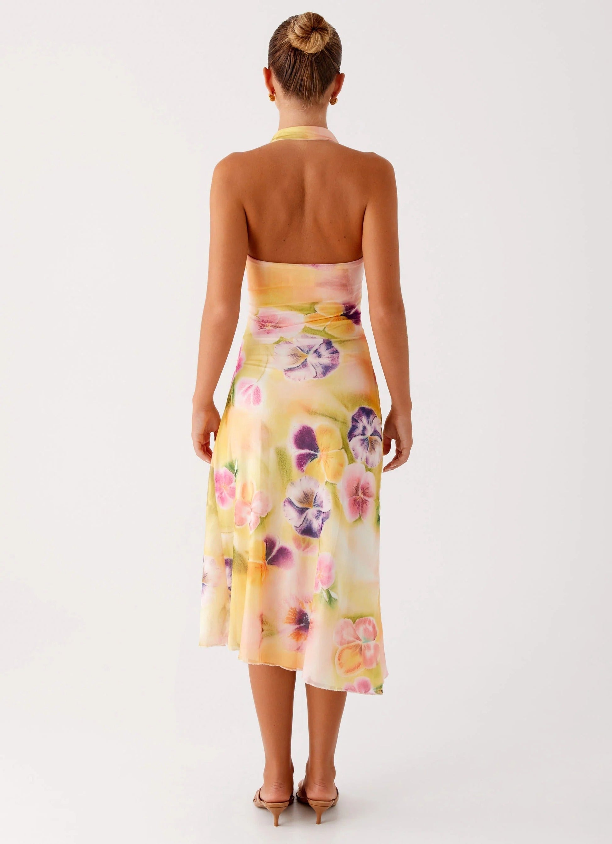 Back view of a woman showcasing the bare back design of the yellow floral halter midi dress for women.
