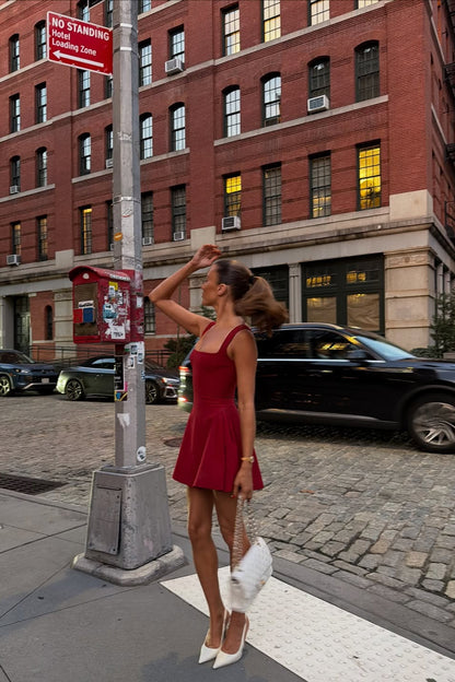 Side profile of the red Lucy skater mini dress, showcasing the full skirt and square neckline, paired with white heels.
