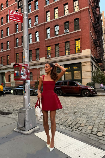 Full view of the red Lucy skater mini dress, with a fitted bodice and flared skirt, accessorized with white heels and a chain strap bag.
