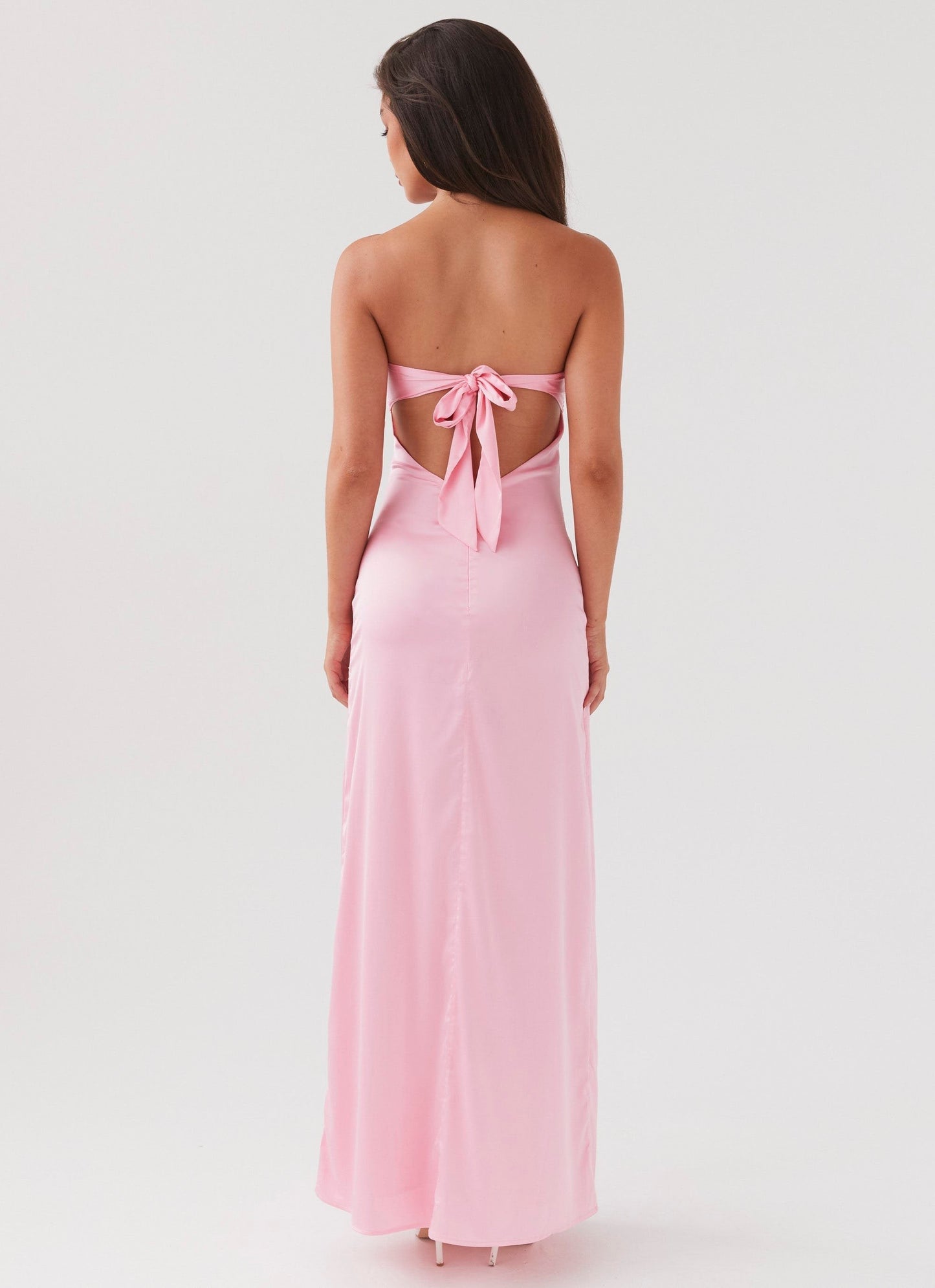 Back view of a strapless pink maxi dress with a bow tie closure and open back detail, flowing to the floor.