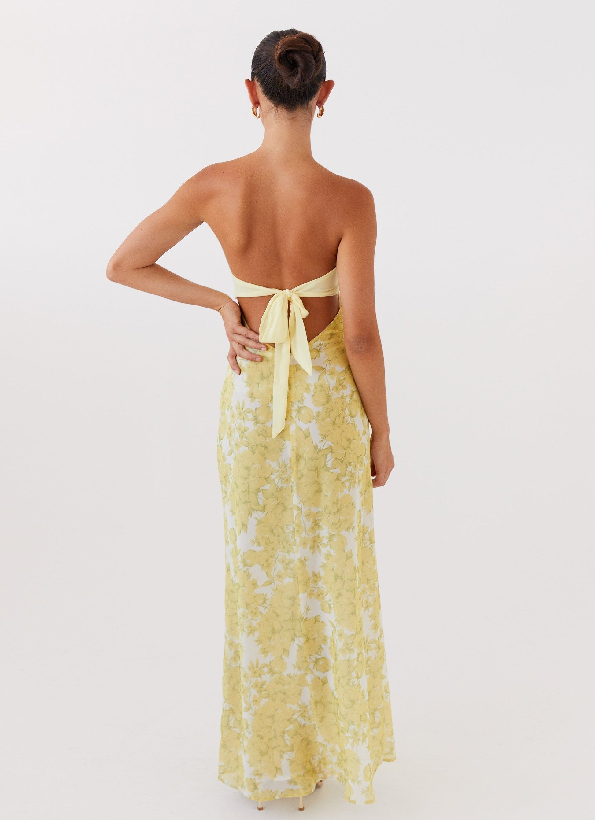 Back view of yellow Lyra Floral Maxi Dress showing tie-back detail and white floral pattern on skirt.