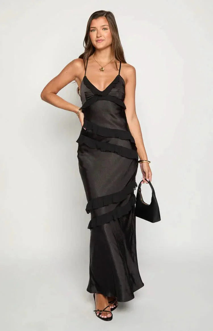 Sleek black Madeline ruffle maxi dress featuring a v-neckline, thin straps, and tiered ruffles, paired with a black handbag.