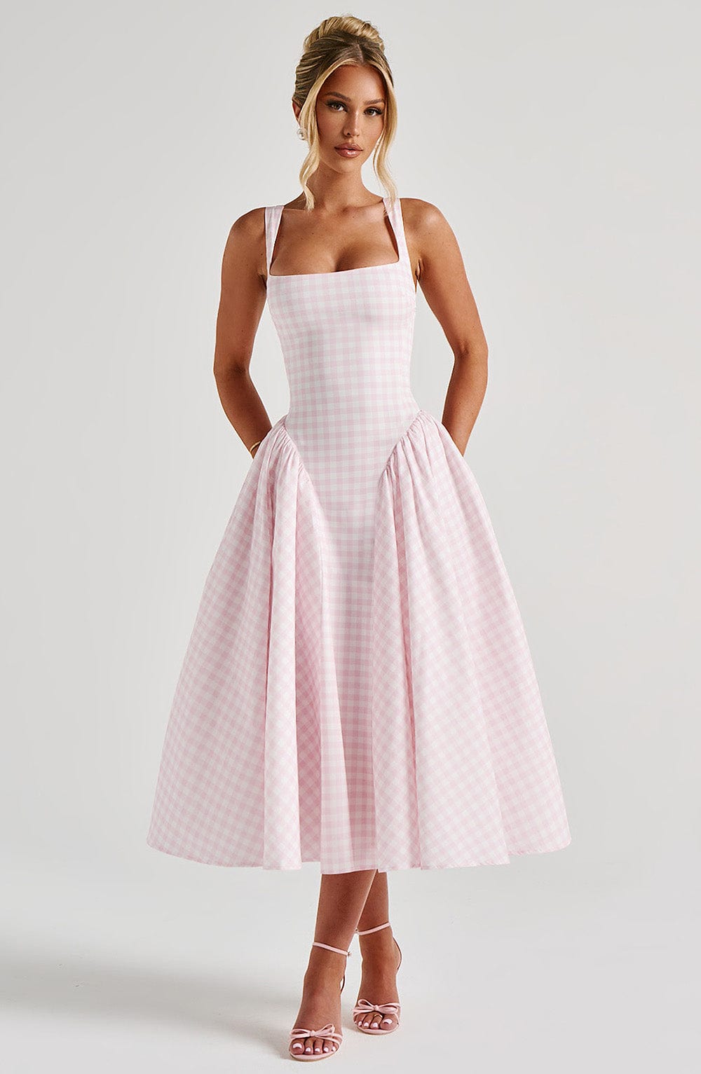 Full body view of a pink gingham midi dress featuring a fitted bodice and gathered skirt, with hands in pockets.