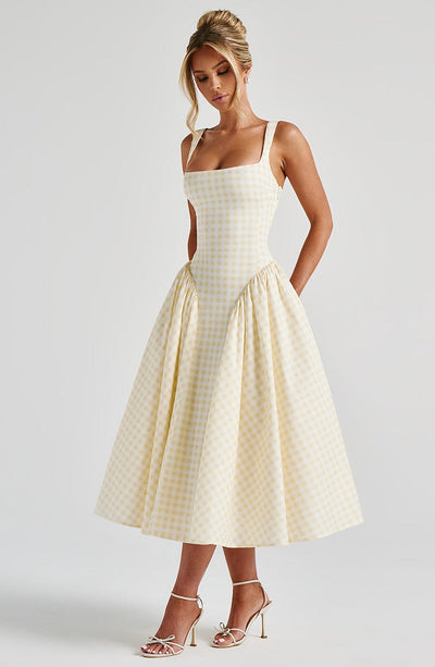 Side profile of a light yellow gingham midi dress with a structured top and a wide, pleated skirt.