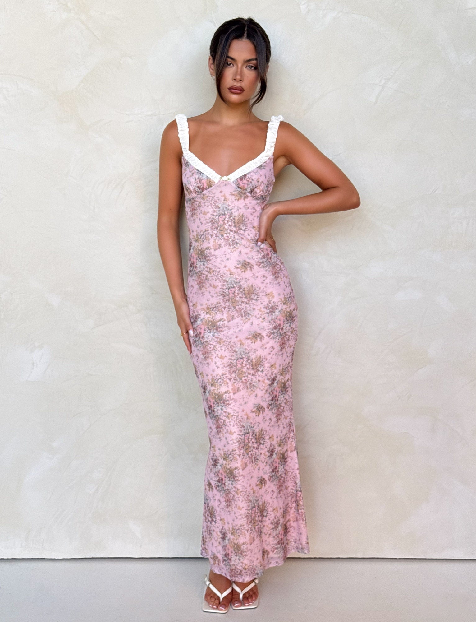 Pink floral maxi dress with white ruffled straps and v-neckline, form-fitting silhouette, perfect for a wedding or event.