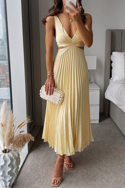 Maria Pleated Maxi Dress in light yellow, featuring a V-neck, side cut-outs, and a flowing pleated skirt, paired with nude heels.