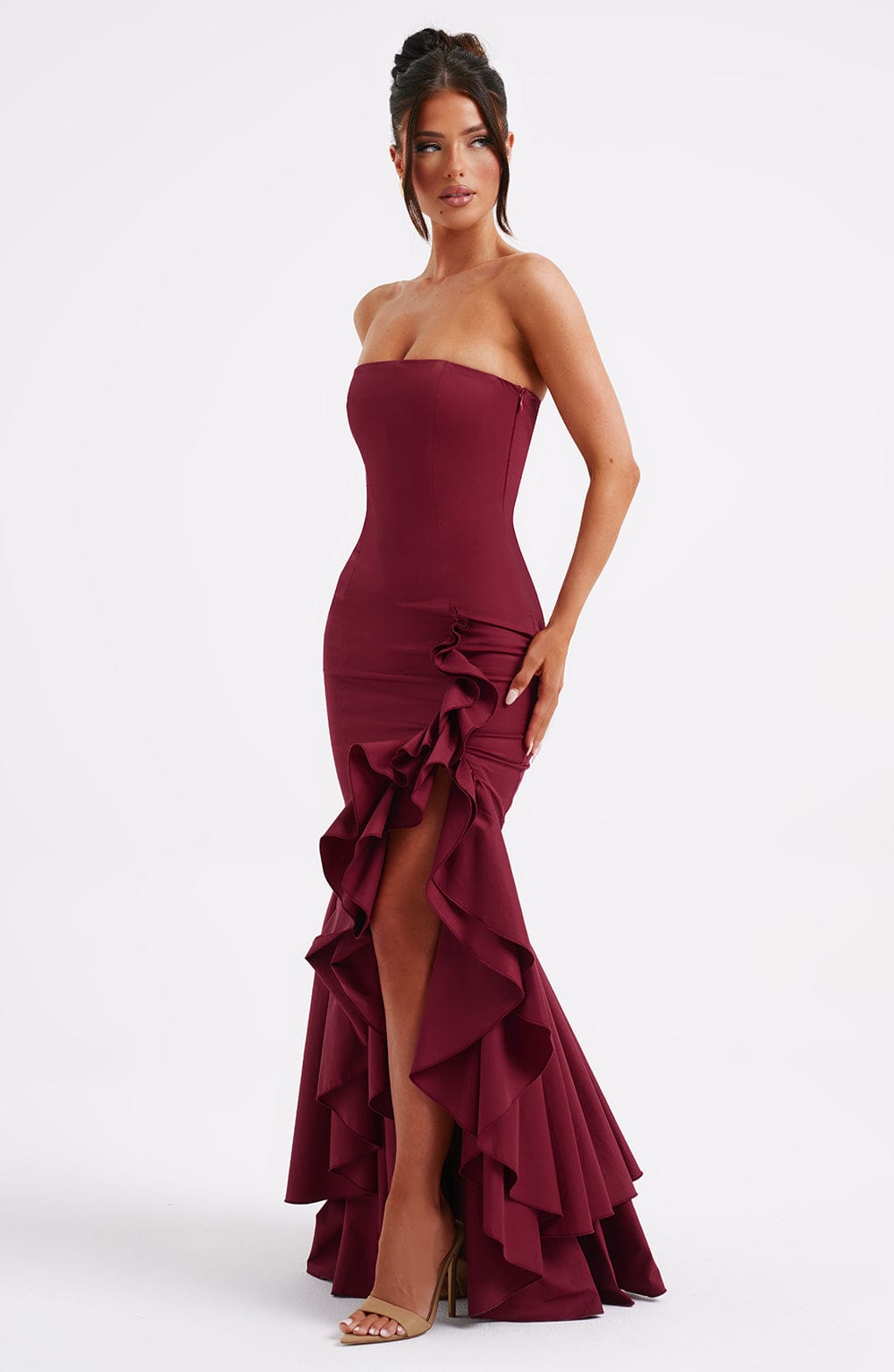 Front-side view of a woman wearing a strapless burgundy Marlowe Ruffle Maxi Dress with a thigh-high slit and ruffles.