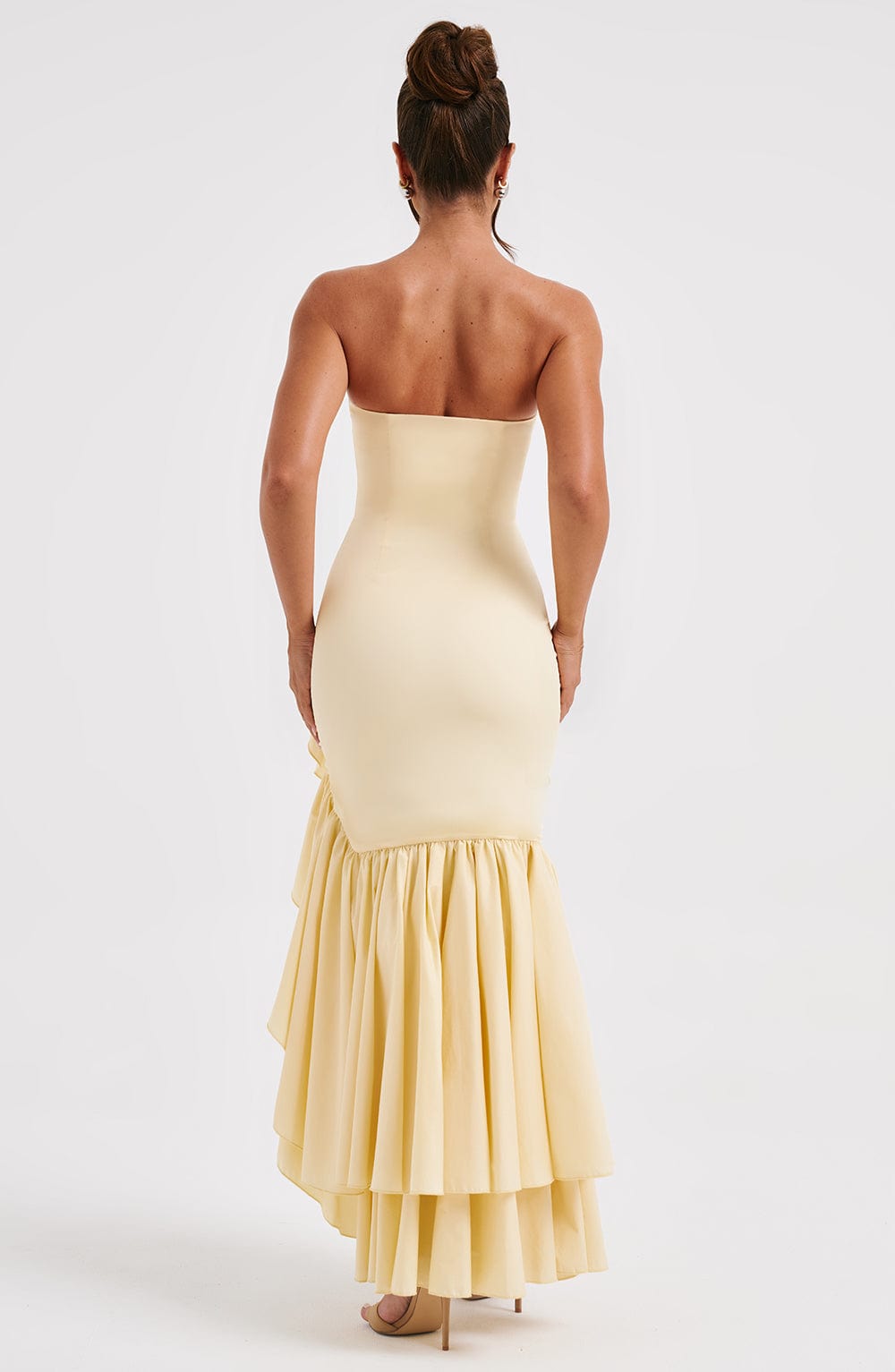 Back view of a woman wearing a strapless light yellow Marlowe Ruffle Maxi Dress, highlighting the tiered ruffled skirt.