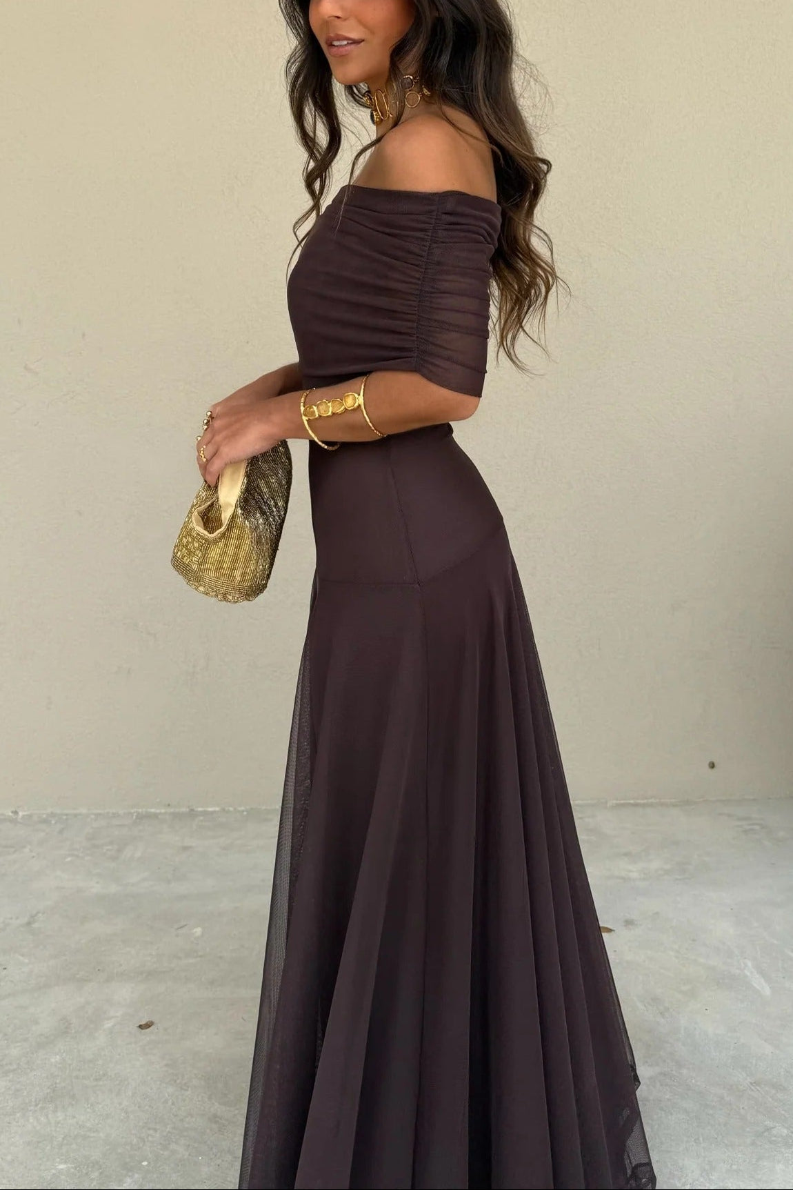 Side view of the dark brown Milena draped maxi dress, highlighting the elegant off-the-shoulder style and full skirt.