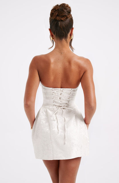 Back view of a white strapless mini dress, showing the corset-style lace-up back and large bow detail.