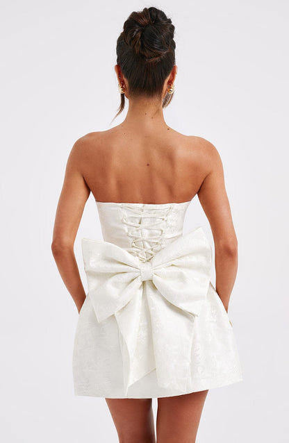 Back view of a white strapless mini dress showcasing a detailed lace-up back and a voluminous bow, a unique suit dress.