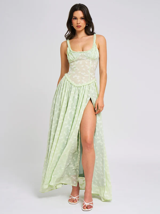 Full-length light green Nina Corset Maxi Dress with a thigh-high slit and delicate floral pattern, paired with white heels.
