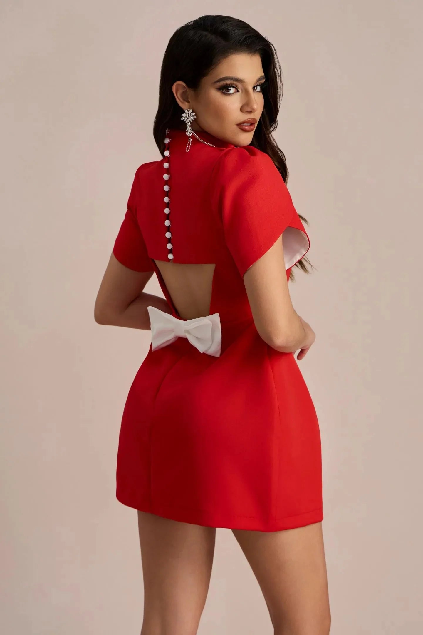 Back view of the red Nora Bow Mini Dress, showcasing pearl buttons, an open back cutout, and a large white bow.