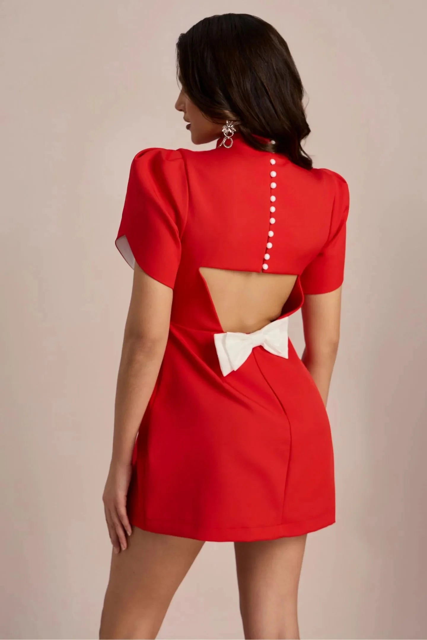 Rear angle of the red Nora Bow Mini Dress, highlighting the pearl button detail, open back, and prominent white bow.