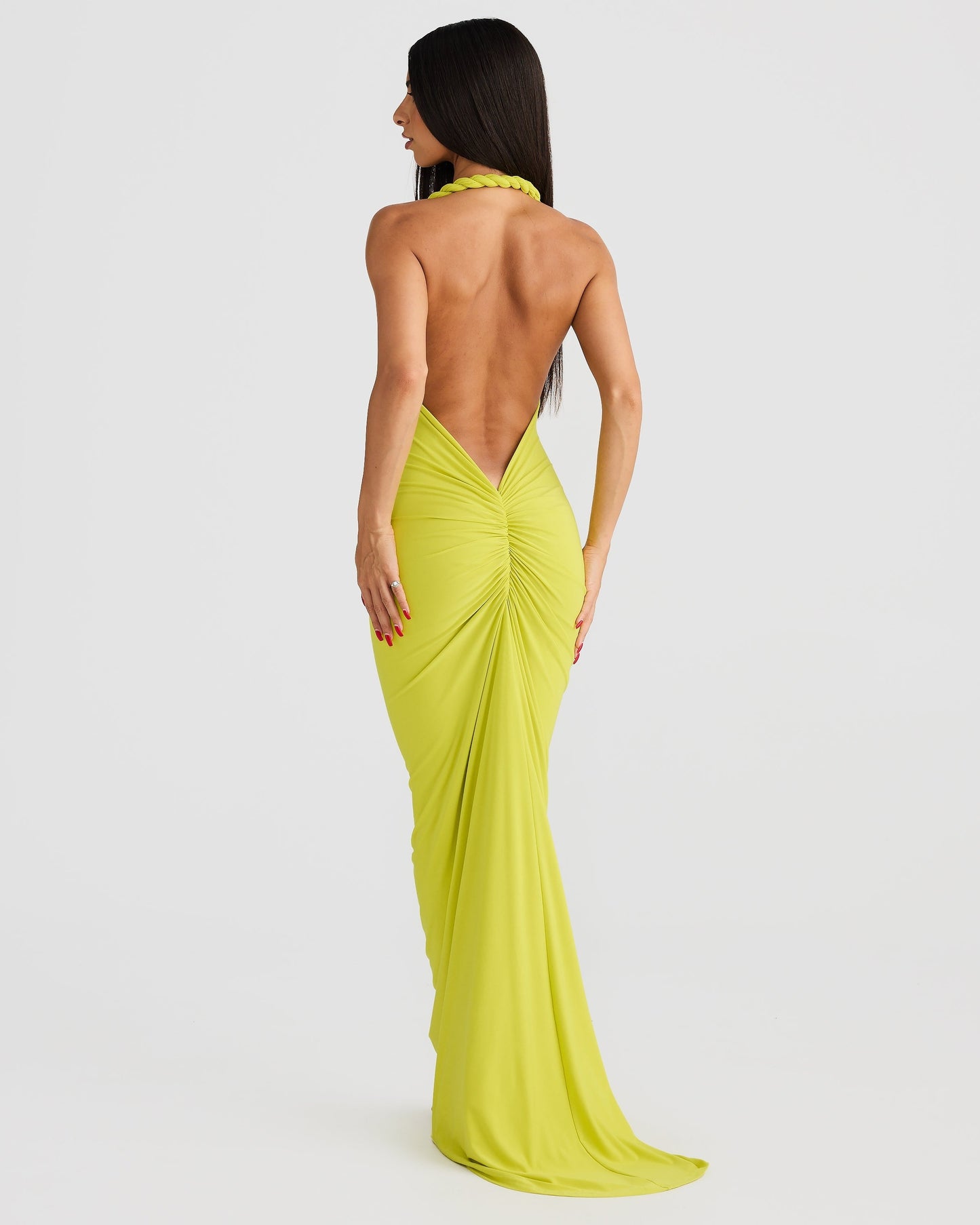 Back view of a woman wearing a floor-length lime green backless maxi dress with ruched detailing on the back.