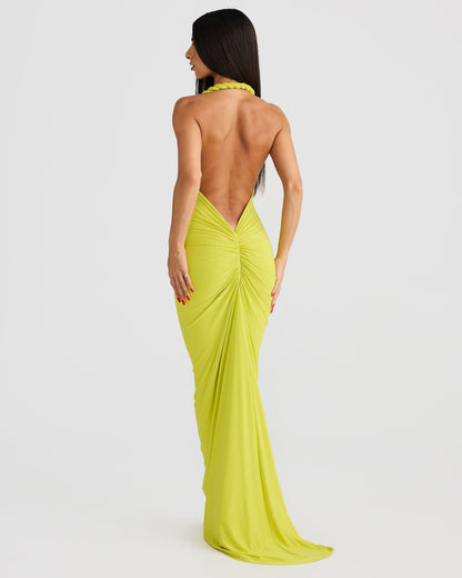 Back view of a woman wearing a floor-length lime green backless maxi dress with ruched detailing on the back.