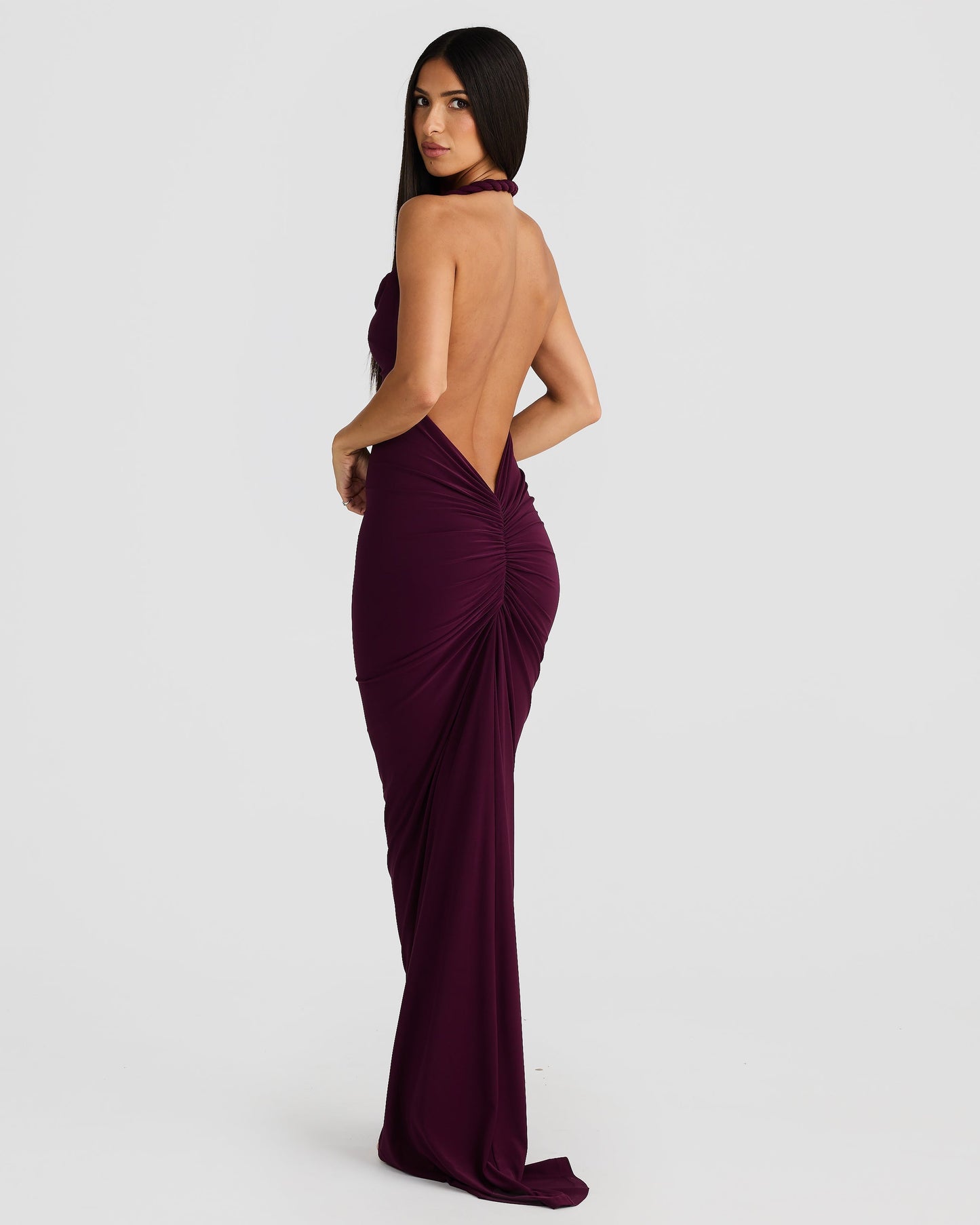 Back view of a woman in a plum purple Paulina backless maxi dress with a halter neckline and elegant ruched detail.