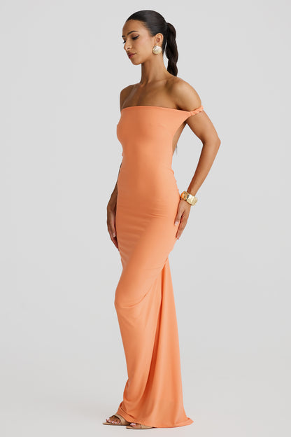 Side profile of a peach Paulina backless maxi dress featuring a draped off-the-shoulder neckline and flowing skirt.