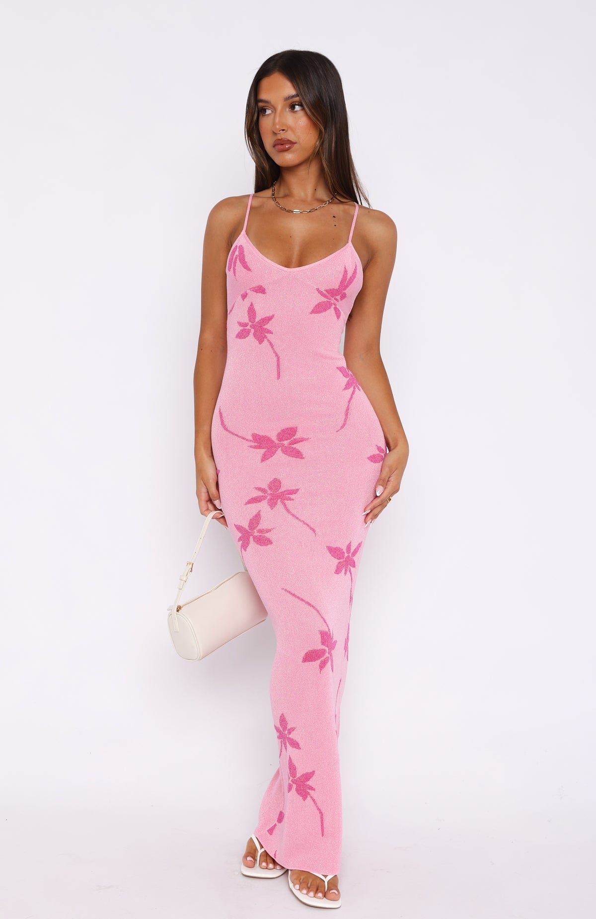 Full-length view of a woman wearing a pink Rebekah Floral Maxi Dress with prominent dark pink floral patterns, holding a white shoulder bag.