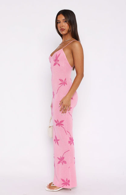 Side profile of a woman in the pink Rebekah Floral Maxi Dress, emphasizing the bold floral design and form-fitting style, with a white handbag.