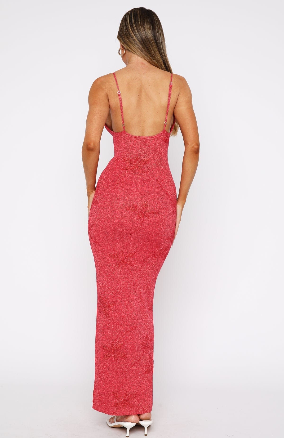 Rear view of a woman in the red Rebekah Floral Maxi Dress, showcasing the back design and the subtle sparkle of the fabric, with white thong heels.