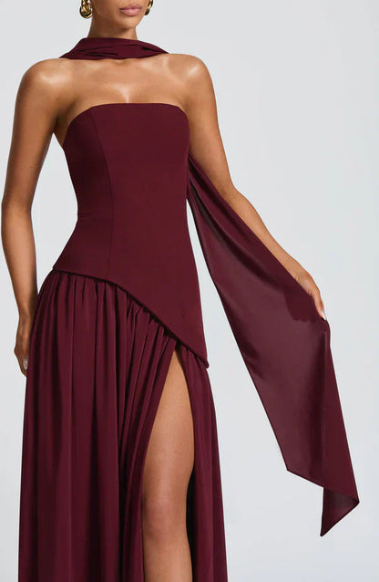 Close-up of a deep burgundy Rhea Asymmetrical Maxi Dress, featuring a strapless bodice, high slit, and flowing fabric detail.