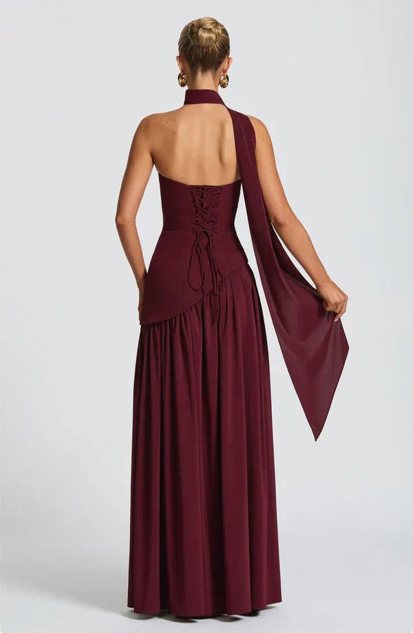 Back view of the burgundy Rhea Asymmetrical Maxi Dress, showing the lace-up corset detail and flowing fabric drape.