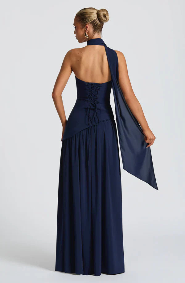 Rear view of the navy blue Rhea Asymmetrical Maxi Dress, showcasing the corset-style lacing and long flowing scarf detail.
