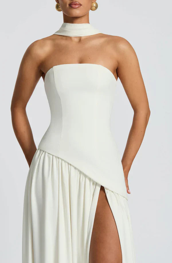 Detailed front view of the ivory Rhea Asymmetrical Maxi Dress, showing the fitted bodice and pleated skirt with a high slit.
