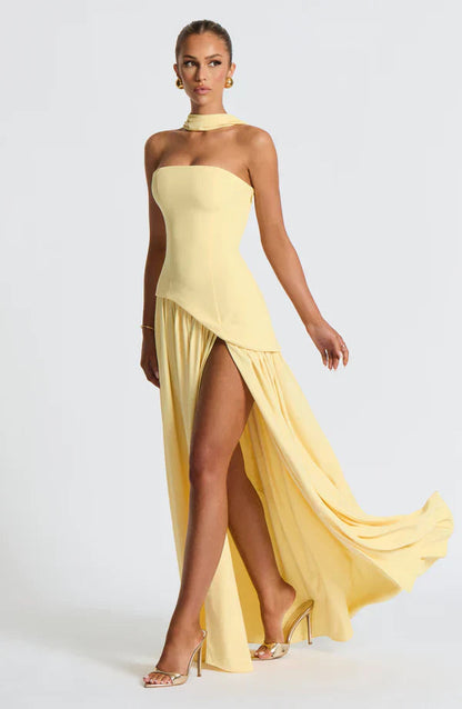 Full body shot of a light yellow Rhea Asymmetrical Maxi Dress, featuring a strapless silhouette, high slit, and choker neck.
