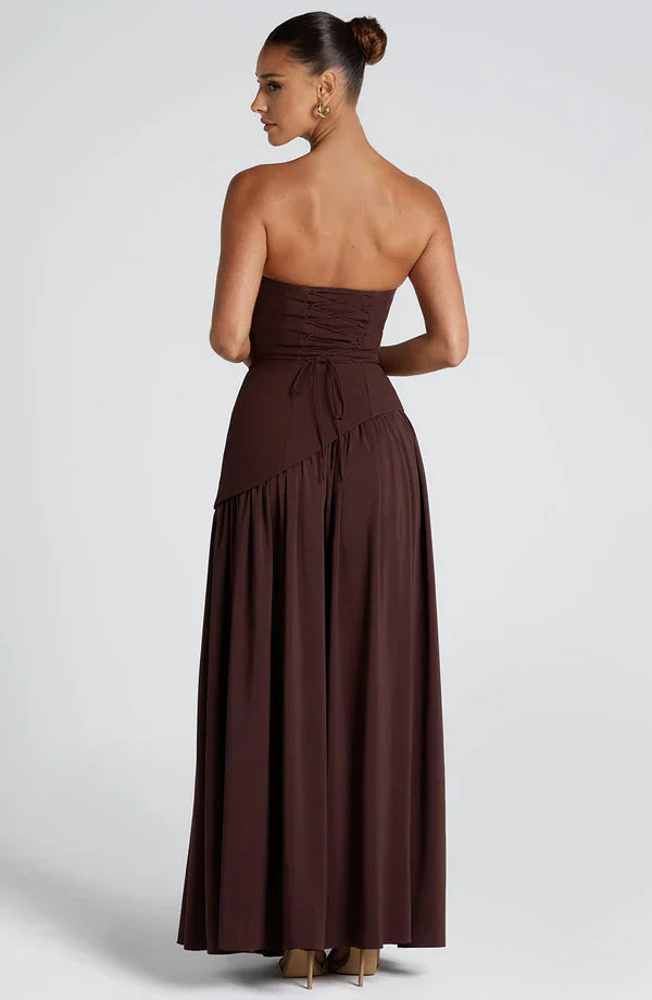 Back view of the dark brown Rhea maxi dress, highlighting the corset-style lace-up back and long skirt.