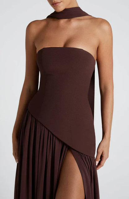 Close-up of the dark brown strapless bodice and pleated skirt detail of the Rhea asymmetrical maxi dress.