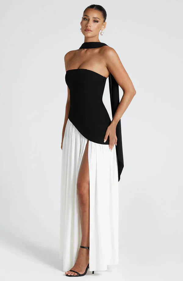 Full-length black and white asymmetrical maxi dress with a strapless black bodice and flowing white pleated skirt with a high slit.