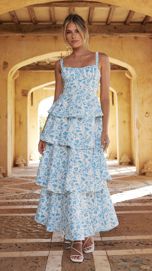 Front view of a white maxi dress with blue floral print, tiered skirt, and square neckline, worn with white heels.
